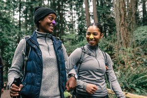 Two beautiful, cool women each wearing colorful Nöz sunscreen on their noses as they hike in a beautiful forest.